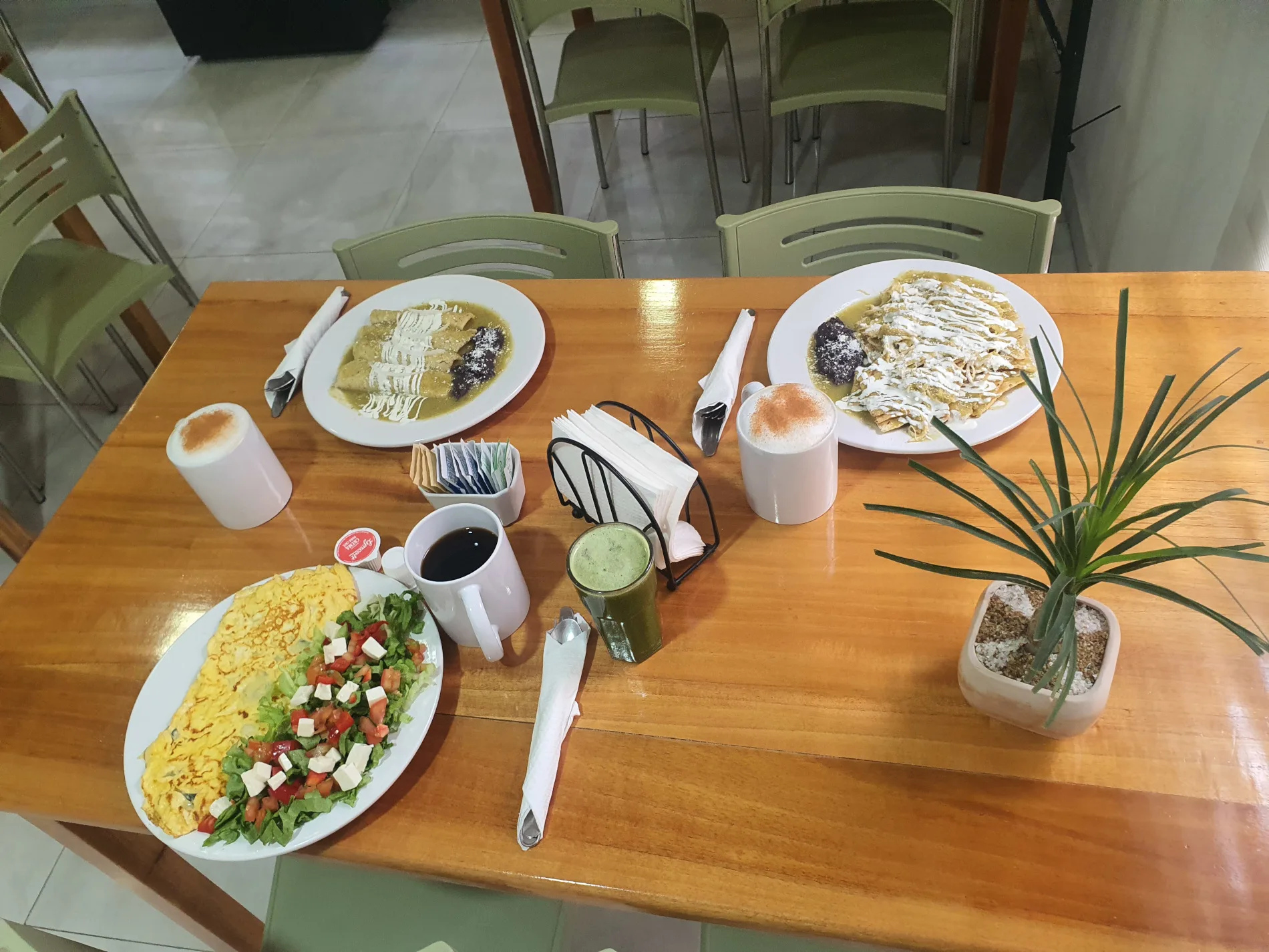 Desayuno servido en mesa de madera diferentes platillos en Kass Bakery & Restaurant, incluye jugos de naranja, enchiladas suizas, enchiladas rojas